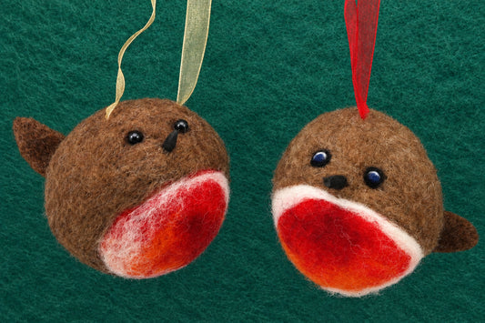Two handmade felt bird ornaments hanging against a dark green textured background. One ornament has a gold ribbon and the other has a red ribbon, both made of brown felt with red and white beaks and black bead eyes.