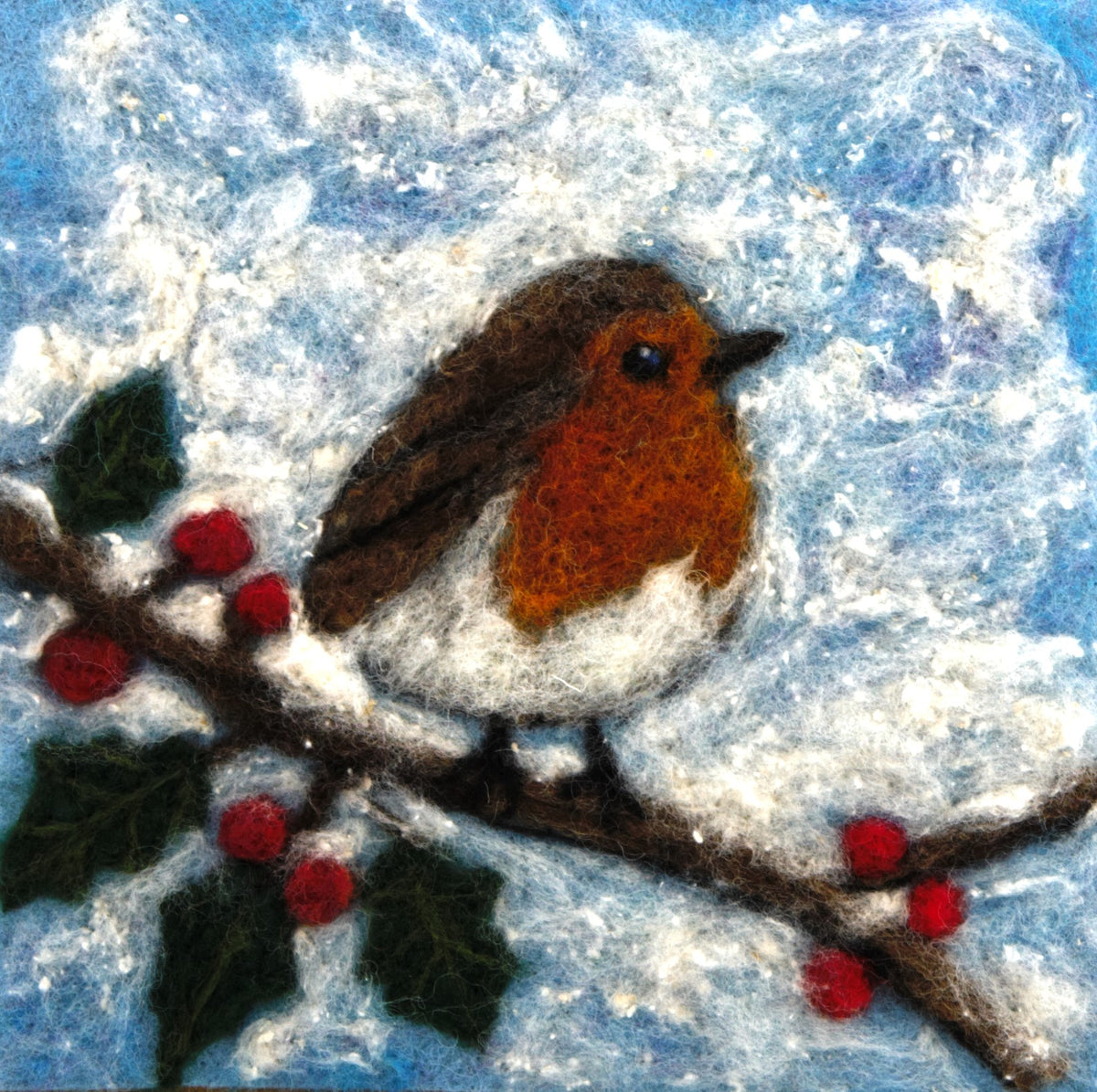A felted wool art piece depicting a robin bird perched on a snowy branch with red berries against a blue and white winter sky.