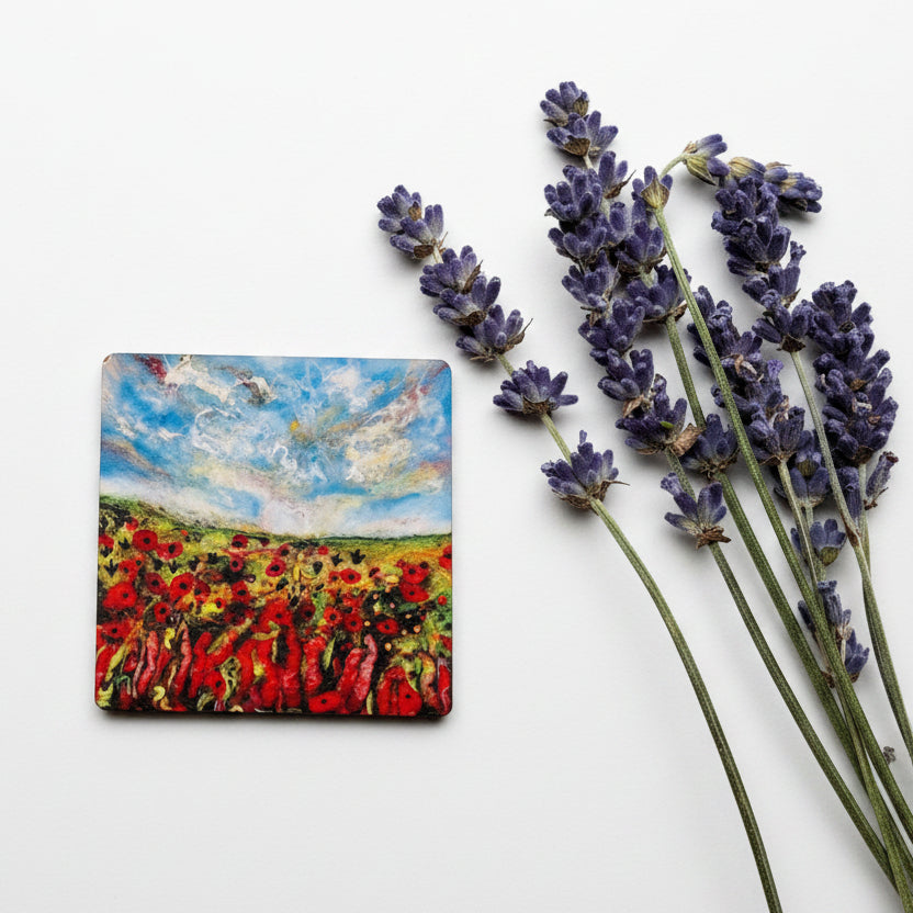 A small square canvas painting depicting a vibrant poppy field under a blue sky, styled on a textured gray concrete surface next to sprigs of purple lavender.