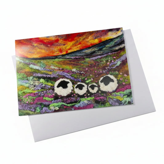 A square art print or greeting card with a colorful landscape painting of three sheep, placed on a white envelope 