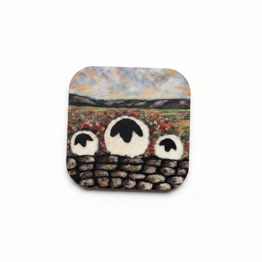 A square ceramic tile coaster featuring a hand-painted design of three sheep in a field, styled on a textured gray concrete surface next to sprigs of lavender.