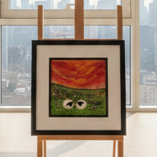 A framed colorful artwork displayed on a wooden easel outdoors against a stone wall and trees.