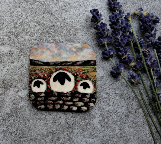A square handmade stone mosaic piece depicting three sheep in a field, styled on a textured gray concrete surface next to sprigs of lavender.