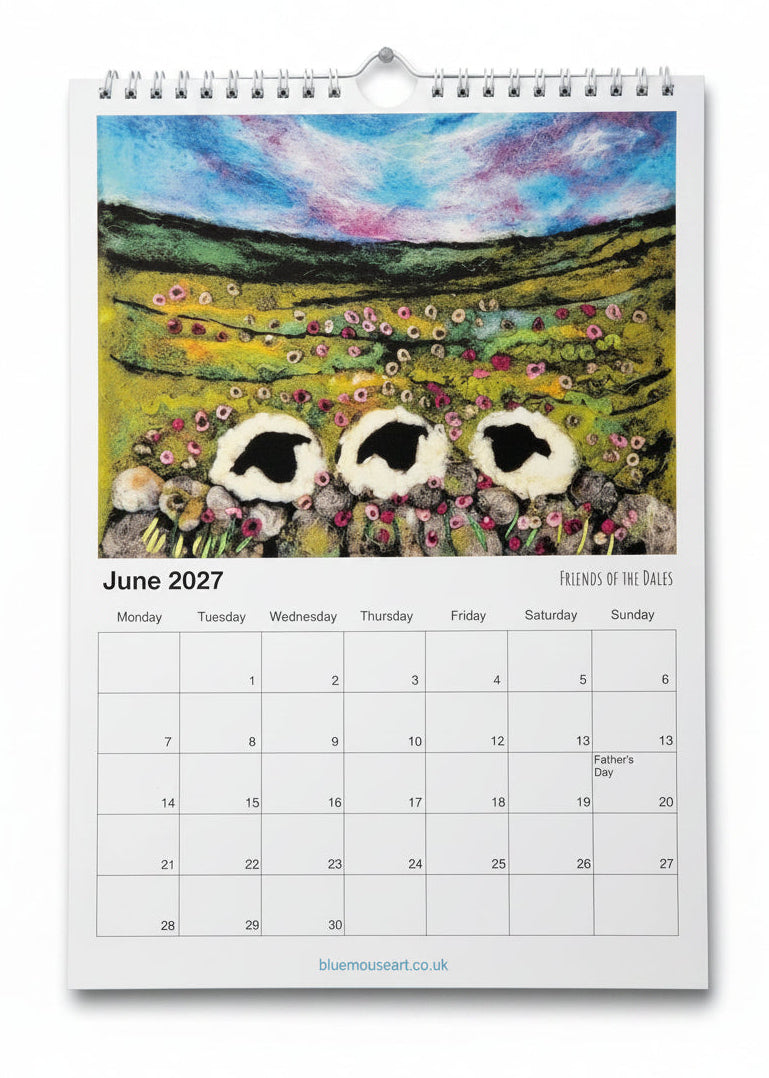 A spiral-bound June 2027 calendar page featuring a colorful painted landscape with three sheep and wildflowers, with a white calendar grid below.