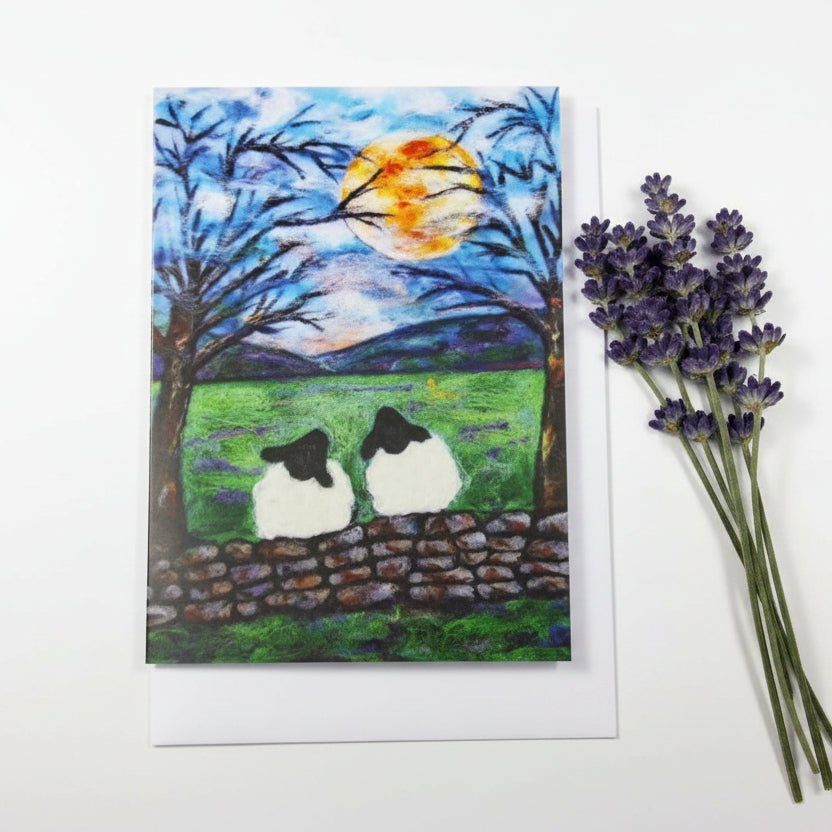 A square art print or greeting card featuring a painted scene of two sheep on a stone wall in a green field under a full moon, 