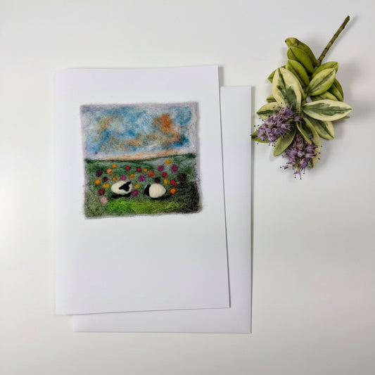 A square felted wool art print featuring a split landscape scene, displayed on a white card over a rustic white wood background with a small decorative plant in the top left corner.
