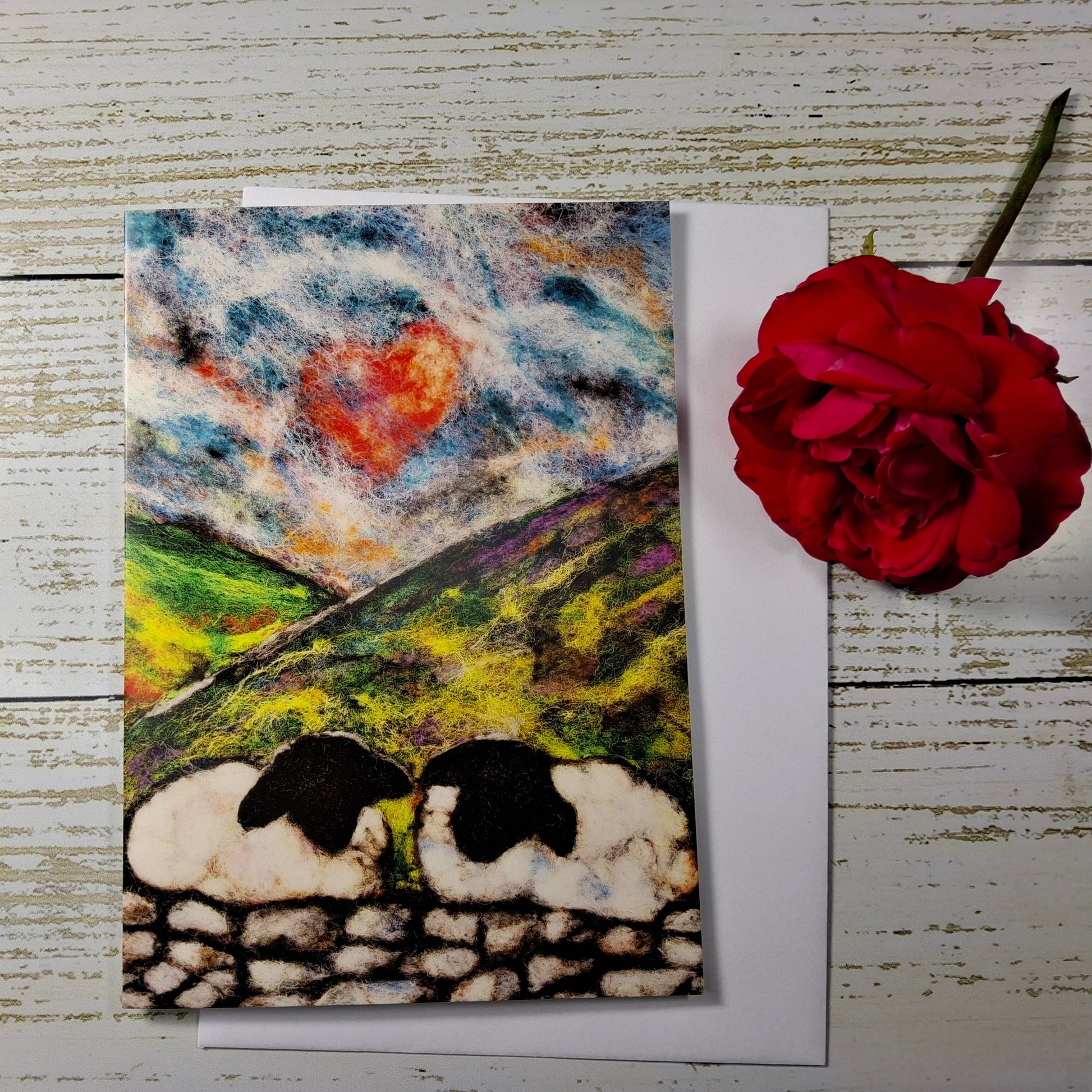 A handmade textured wool art card depicting two sheep in a field under a cloudy sky 