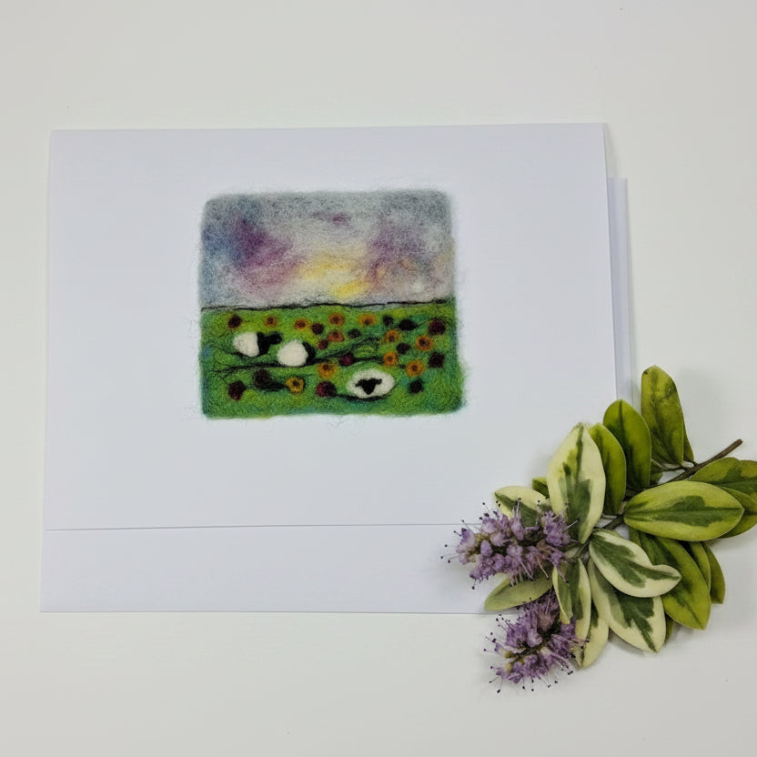 A white square art print or card featuring a small felted wool artwork with a split design: one side is pastel purple, yellow, and blue, and the other is green with small colorful dots and white circular details. The print is photographed on a whitewashed wooden surface with dried flowers in the top corner.