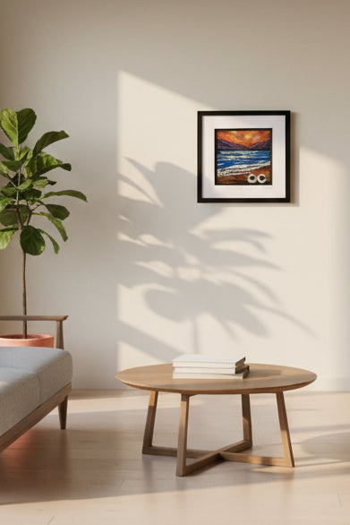 A framed art print depicting a dramatic stormy seascape with a bright orange sky, dark blue waves, and a rocky shore, mounted on a beige wall alongside other framed pictures.