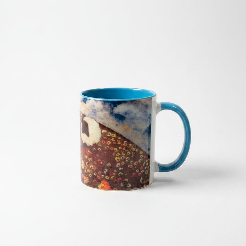A ceramic mug with a blue handle and interior, featuring a printed design of a cat and colorful autumn leaves, sitting on a white wood-plank surface.