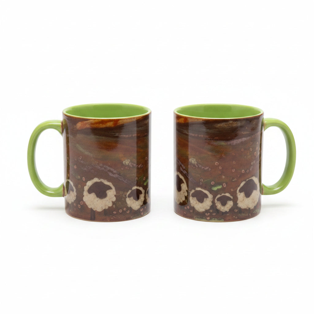 Two ceramic mugs with a brown and black animal print pattern and bright green interiors, displayed on a glass-topped table in a cluttered craft room setting.